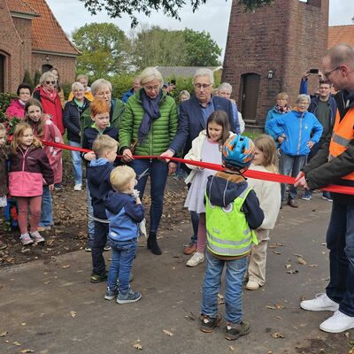 Das Bild zeigt eine Gruppe von Menschen auf dem neuen Radweg. Die Landr&auml;tin Karin Harms durchtrennt das rote Band. Um das rote Band stehen Kinder.