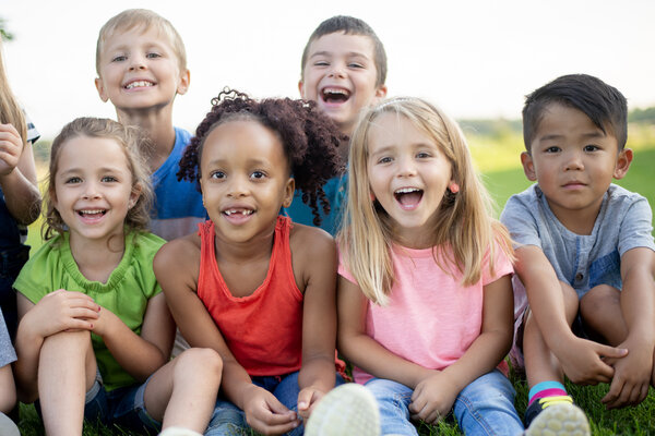A joyful group of diverse kids sitting on a sunny lawn, smiling at the camera, showcasing friendship, laughter, and outdoor play.