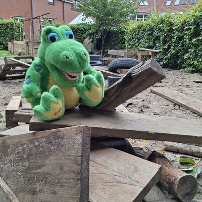 Bild vergr&ouml;&szlig;ern: Maskottchen Kroko im Waldkindergarten auf einem Holzhaufen