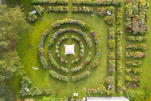 Luftaufnahme einer Gartenanlage mit zahlreichen farbenfrohen Dahlienbeeten, darunter kreisförmig angeordnete Beete.